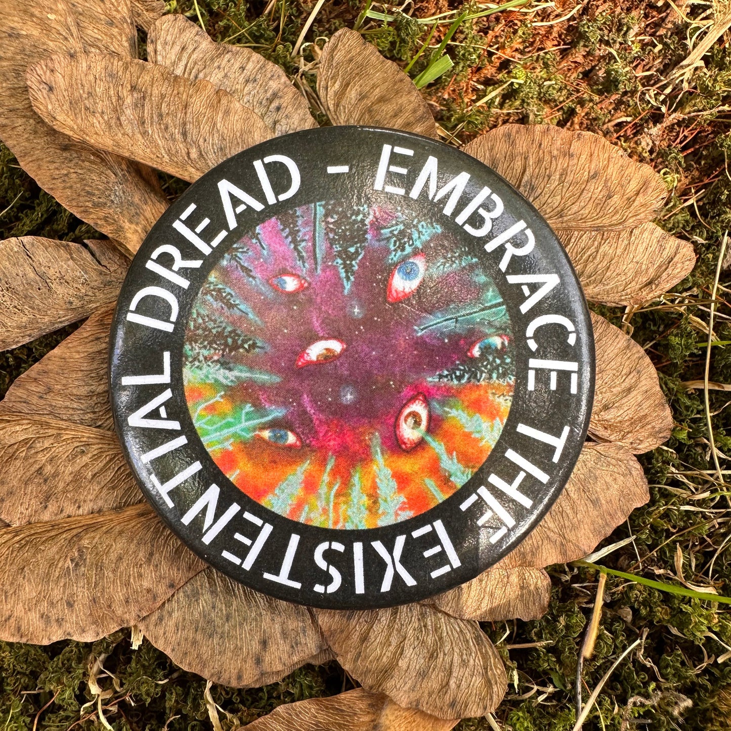 Circle pin with Embrace the Existential Dread encircling the edge. Center features a forest night sky with eyes looking down