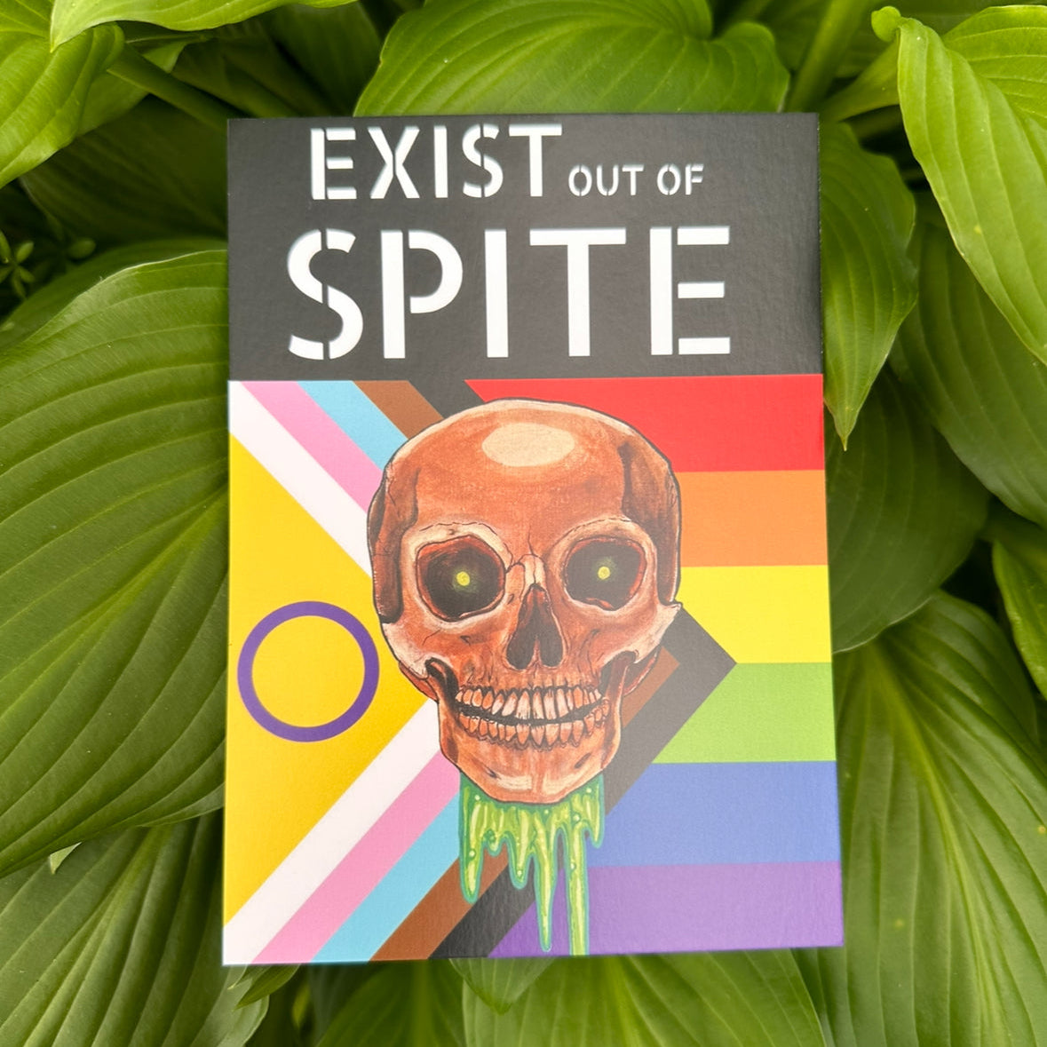 Print with a skull over a pride flag with the text exist out of spite