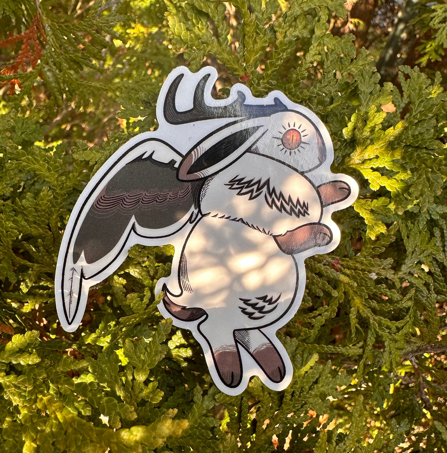 A vinyl sticker depicting a whimsical creature with horns and wings, placed against a foliage background.