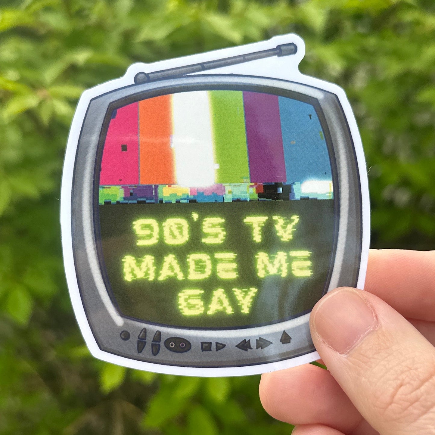 Sticker of a TV with text held by a hand against a green leafy background
