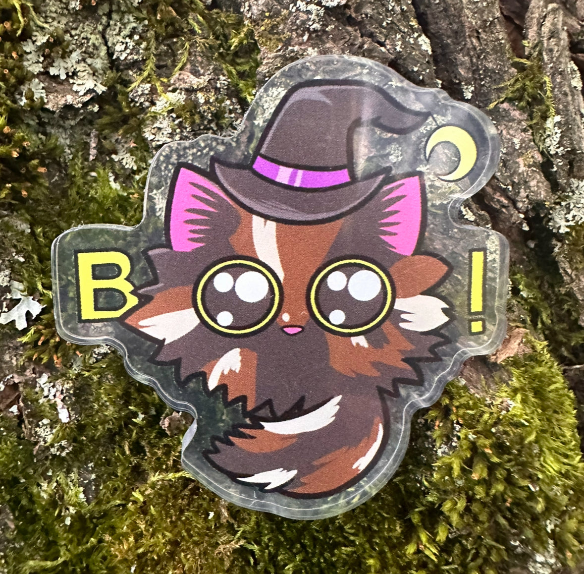 Pin of a cat-like character with a witch hat and eyes used to spell the word ‘boo’ on a textured background