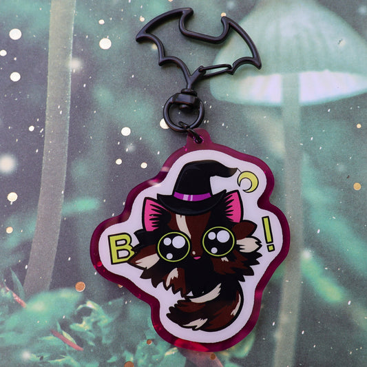 Tortoiseshell cat with Boo spelled with big eyes, purple acrylic background, black bat clasp, keychain.