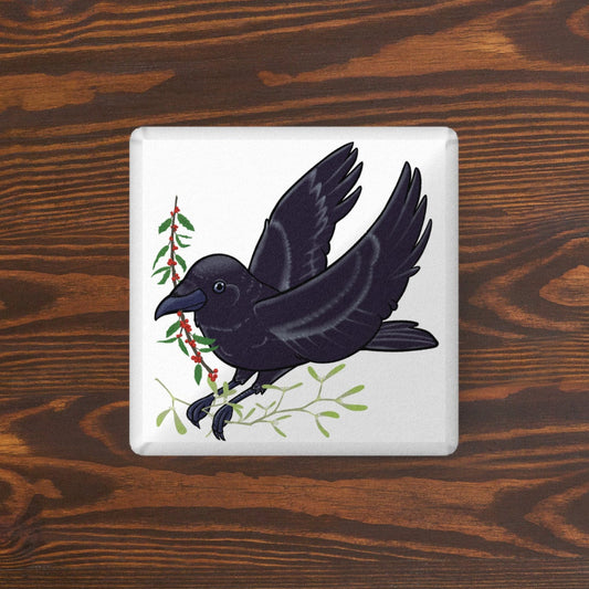 A square-shaped pillow with a black crow design on a white background, placed on a wooden surface.