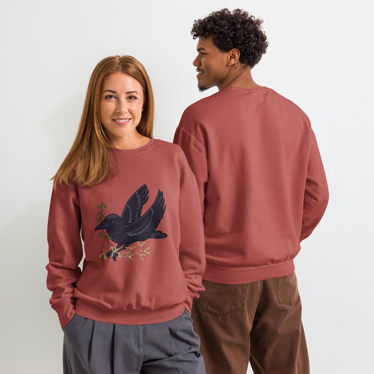Two people wearing matching maroon sweatshirts with a crow design on a plain background