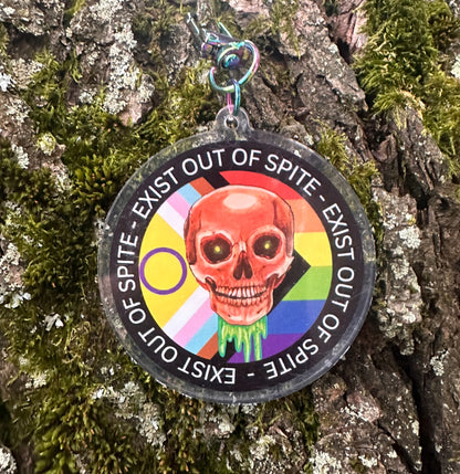 Round keychain with skull design and a pride flag withe words exist out of spite on a tree branch