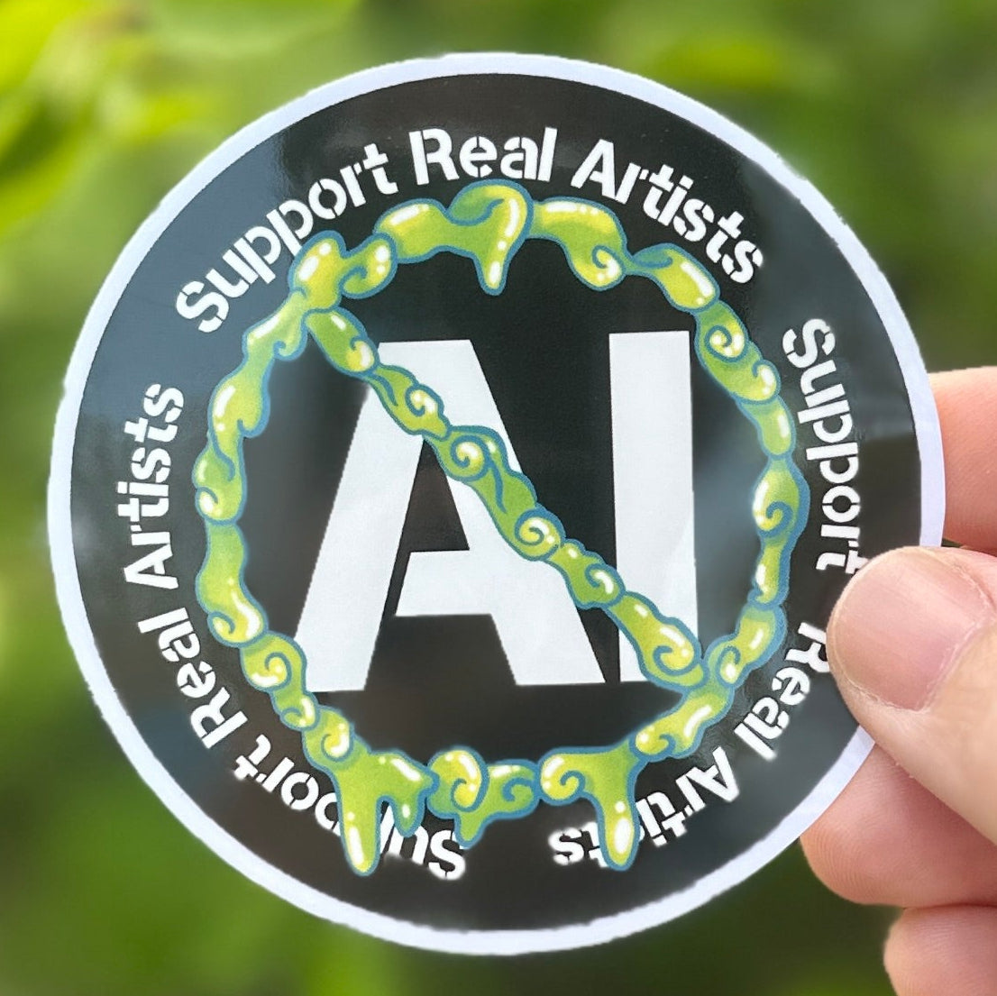 Sticker with Neon green slime forming a no symbol over the text AI encircled by text that says Support Real artists. Background is a green bush.