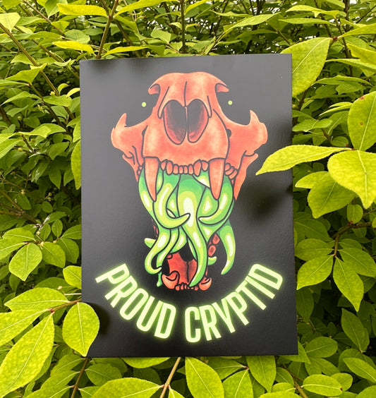 A print featuring a stylized illustration of an animal skull with vibrant orange and green colors, and the text 'Proud Cryptid' below it.