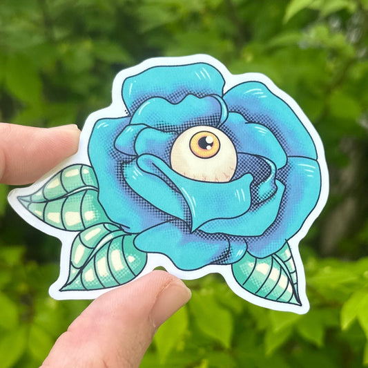 Hand holding a blue flower-shaped sticker in front of green foliage