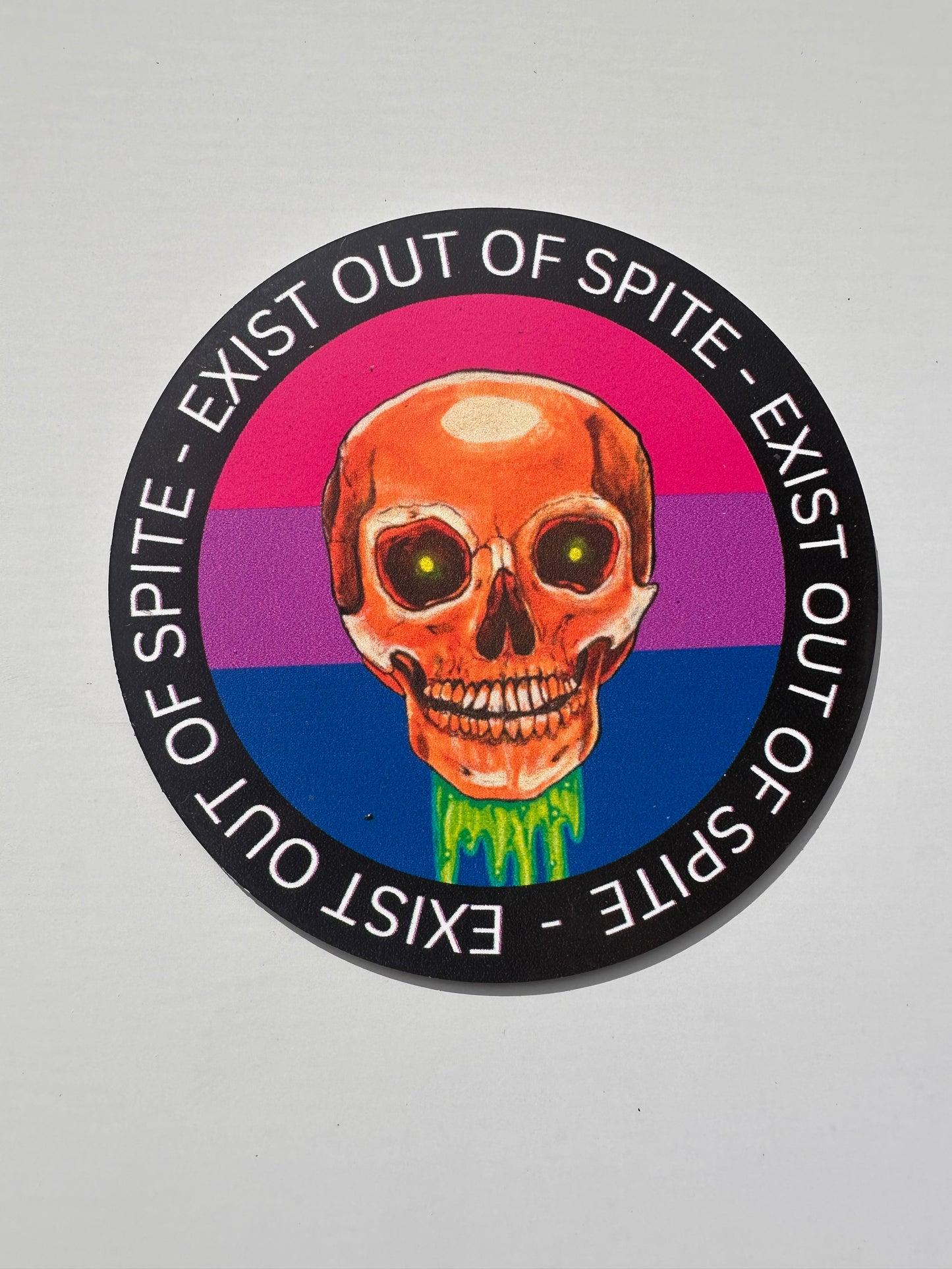 Round magnet with a skull over a bisexual pride flag encircled by the text exist out of spite