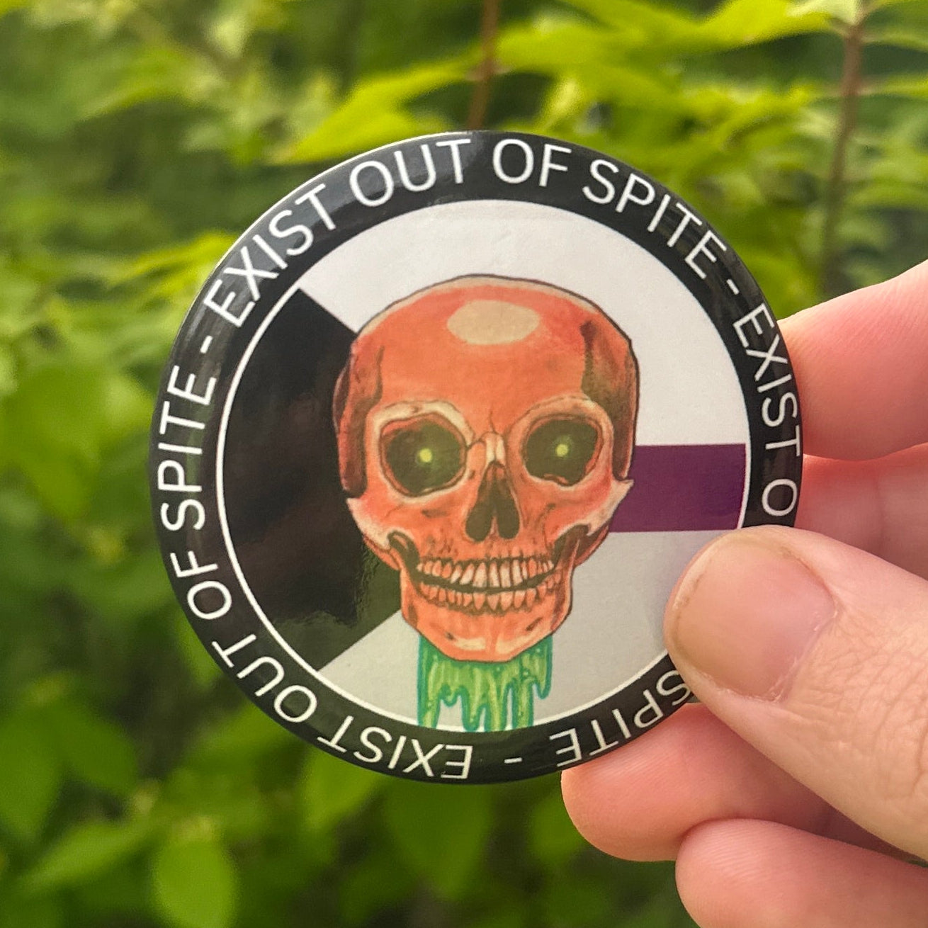 Hand holding a round badge with a skull design against a green leafy background