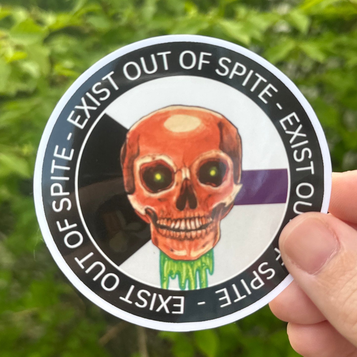 Circular sticker with a skull design held by a hand against a green leafy background