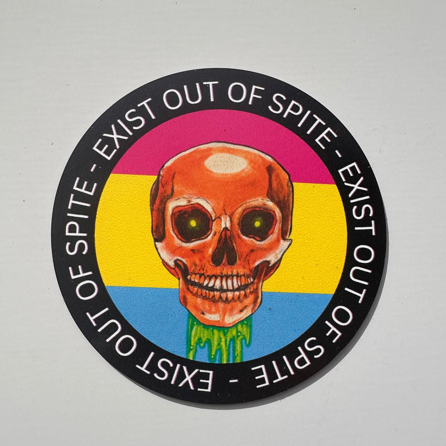Round magnet with a skull over a pansexual pride flag encircled by the text exist out of spite