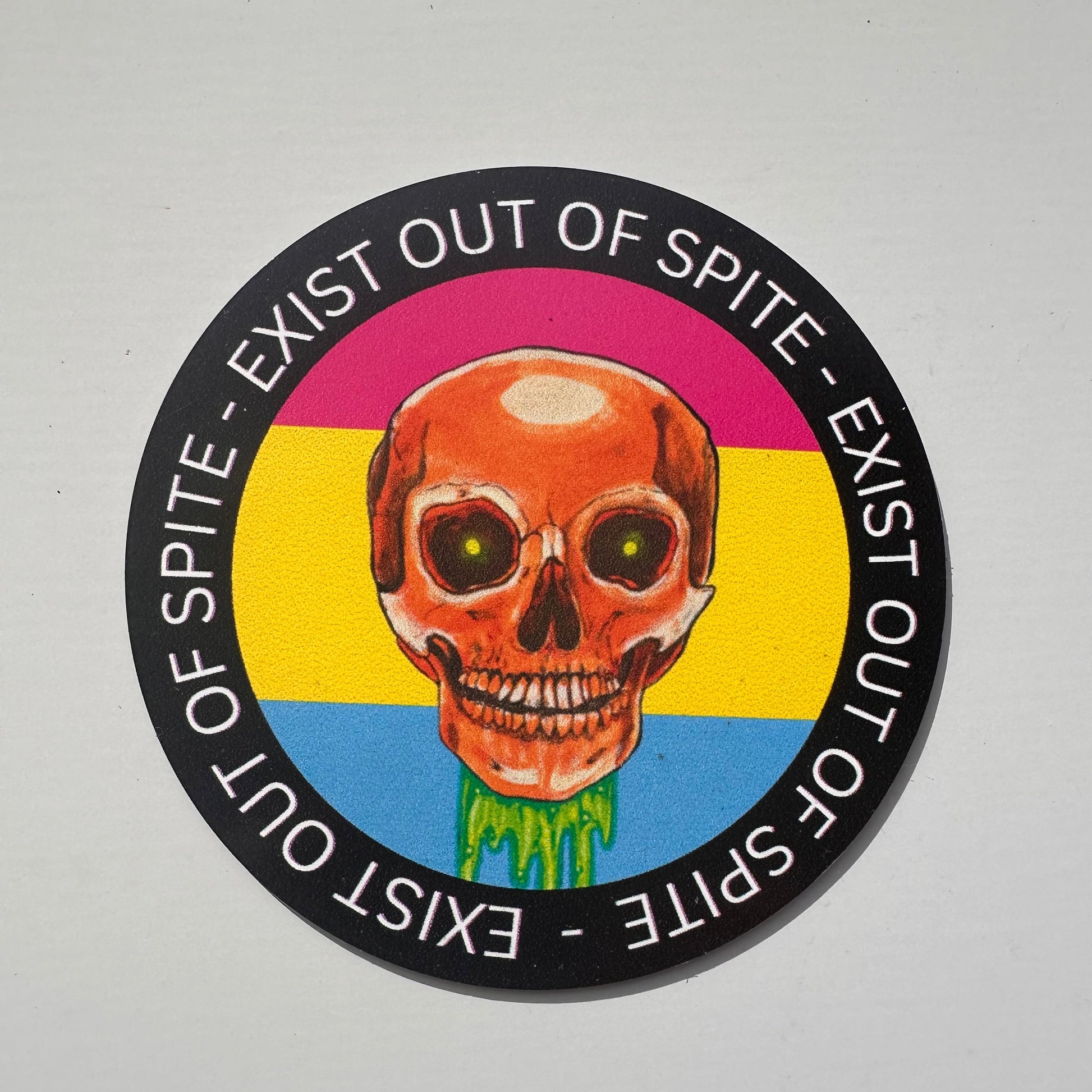 Round magnet with a skull over a pansexual pride flag encircled by the text exist out of spite