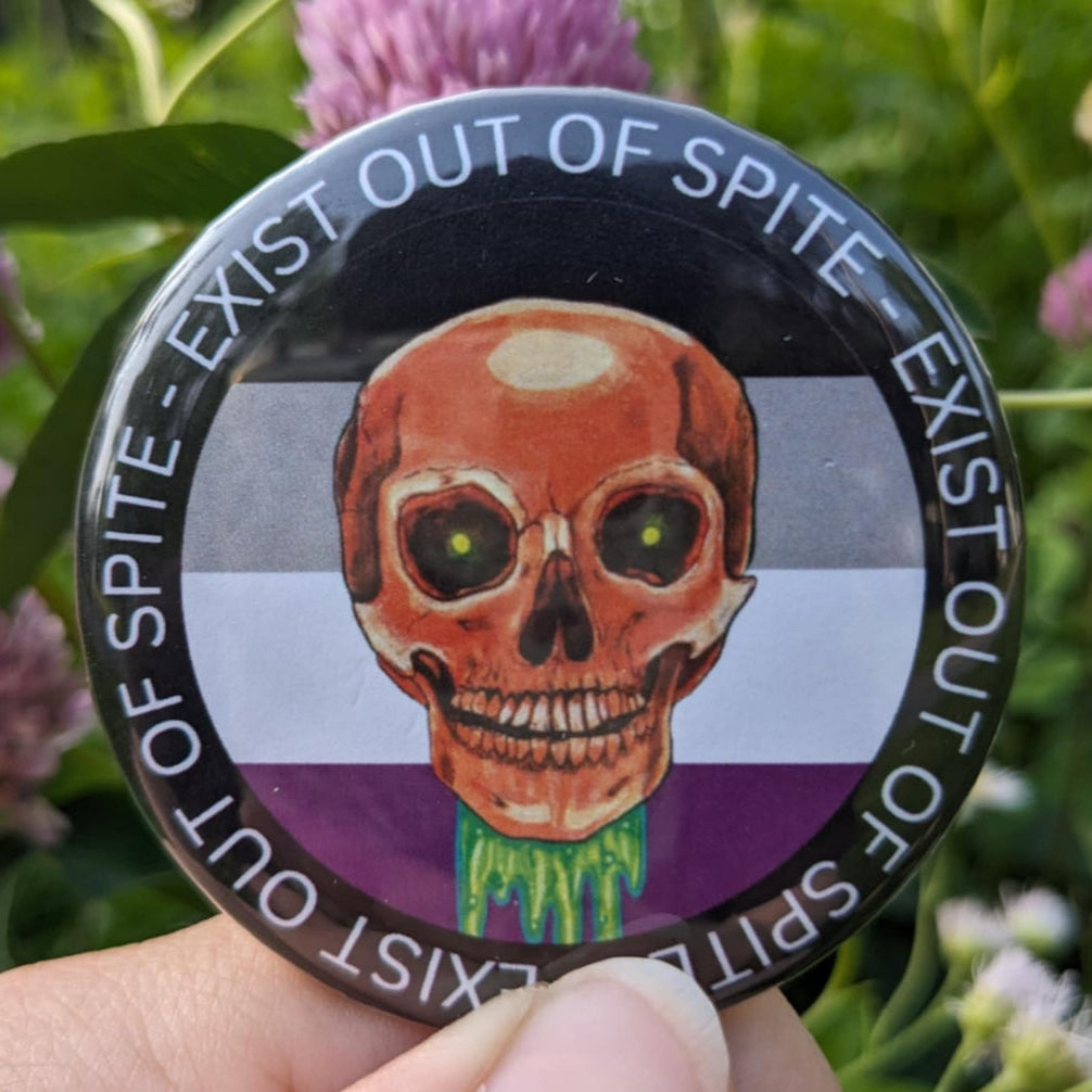 Round pin with a skull over an asexual pride flag encircled by the text exist out of spite