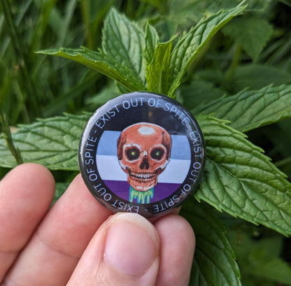 Round pin with a skull over an asexual pride flag encircled by the text exist out of spite