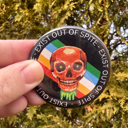 Round pin with a skull over a disabled pride flag encircled by the text exist out of spite