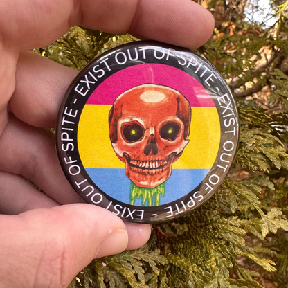 Round pin with a skull over a pansexual pride flag encircled by the text exist out of spite