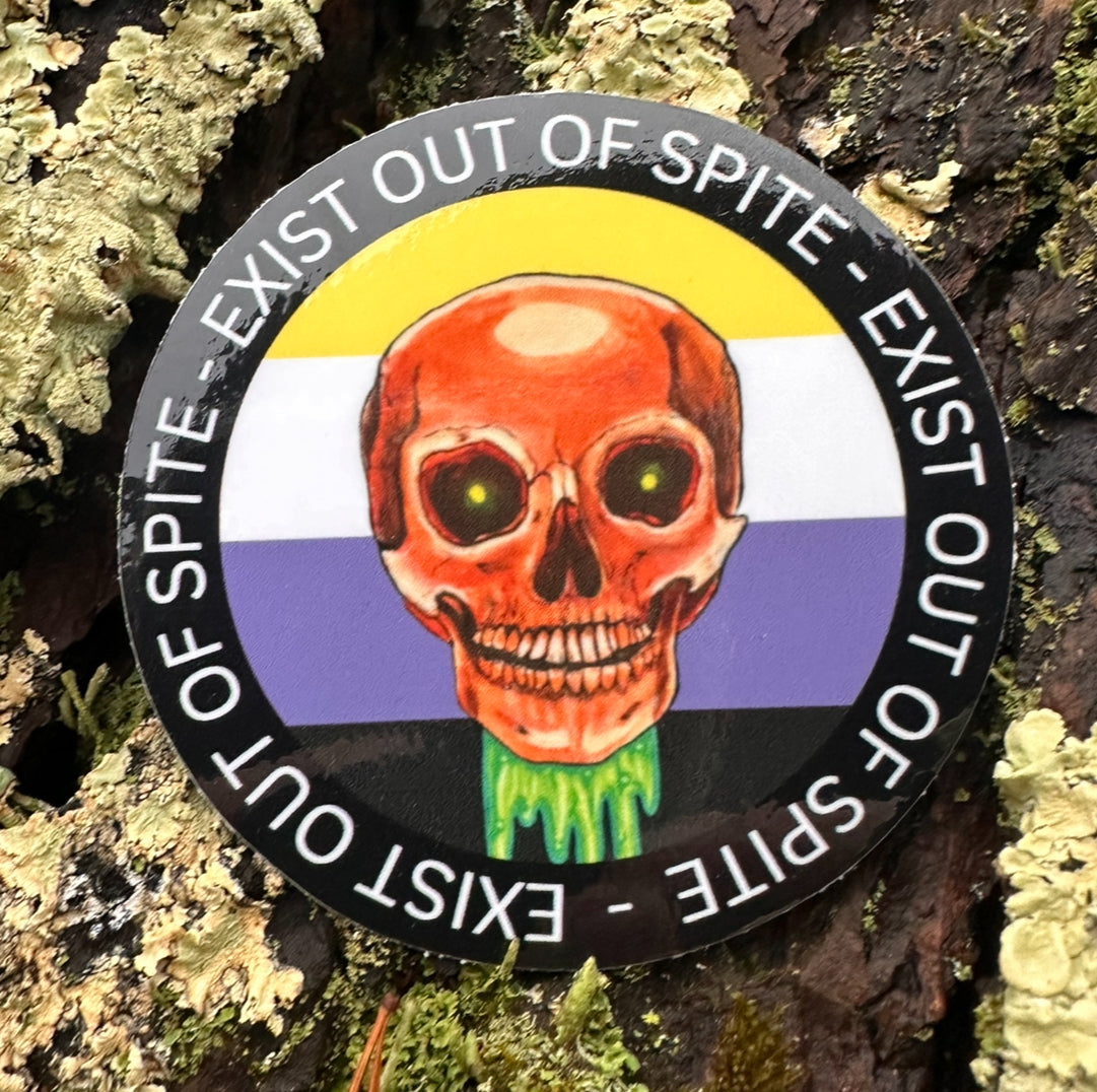 Round sticker with a skull over a nonbinary pride flag encircled by the text exist out of spite