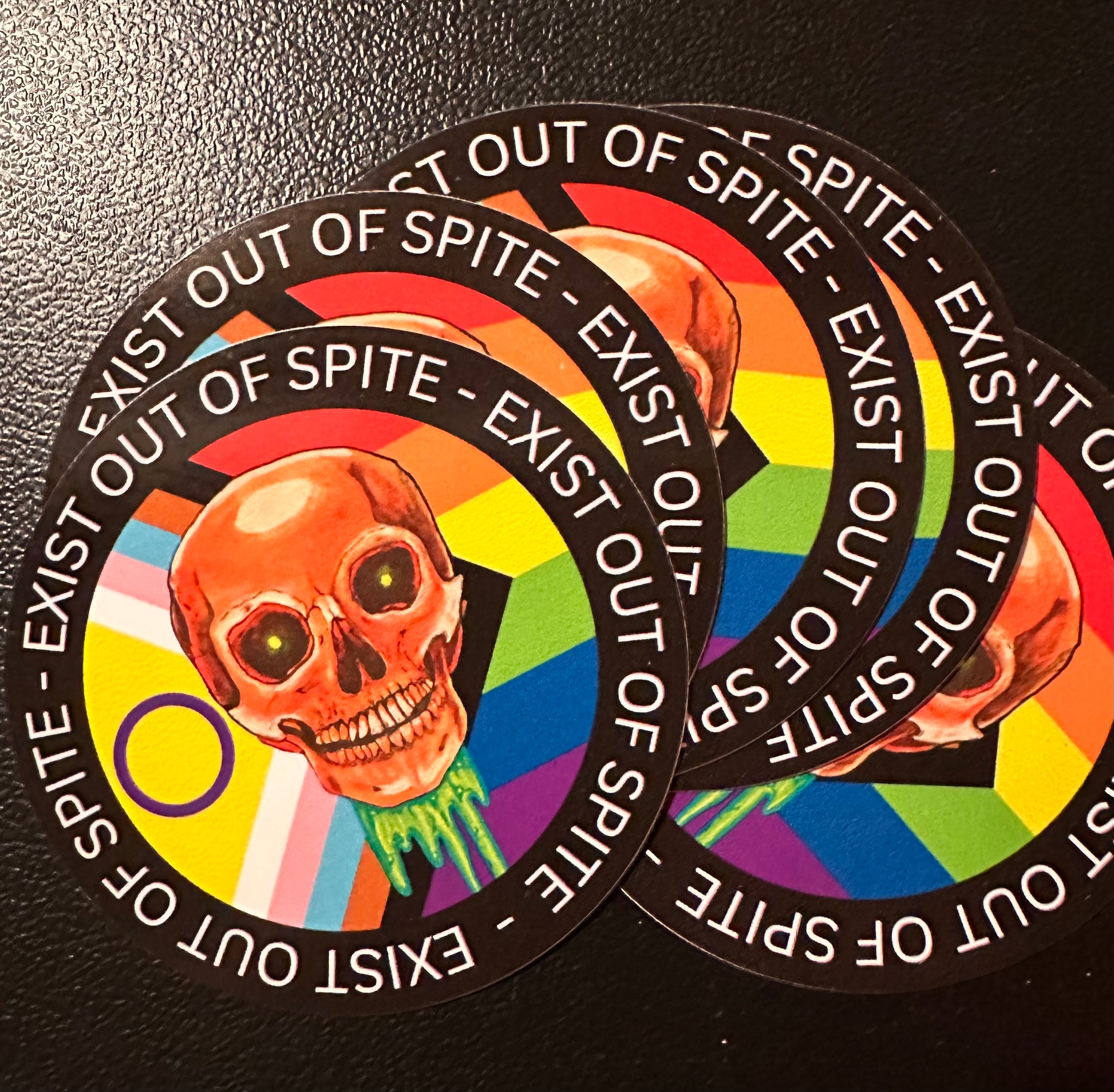 Round sticker 5 pack with a skull over a pride flag encircled by the text exist out of spite