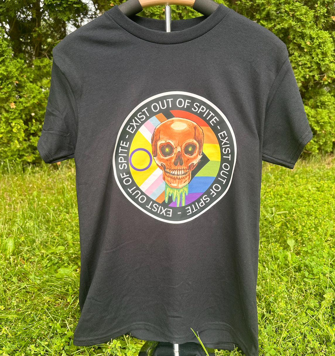 A person wearing a gray 'Exist Out of Spite' T-shirt with a colorful graphic of a skull and text over a pride flag on the front