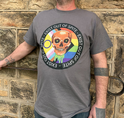 A person wearing a gray 'Exist Out of Spite' T-shirt with a colorful graphic of a skull and text over a pride flag on the front, standing against a stone wall background.