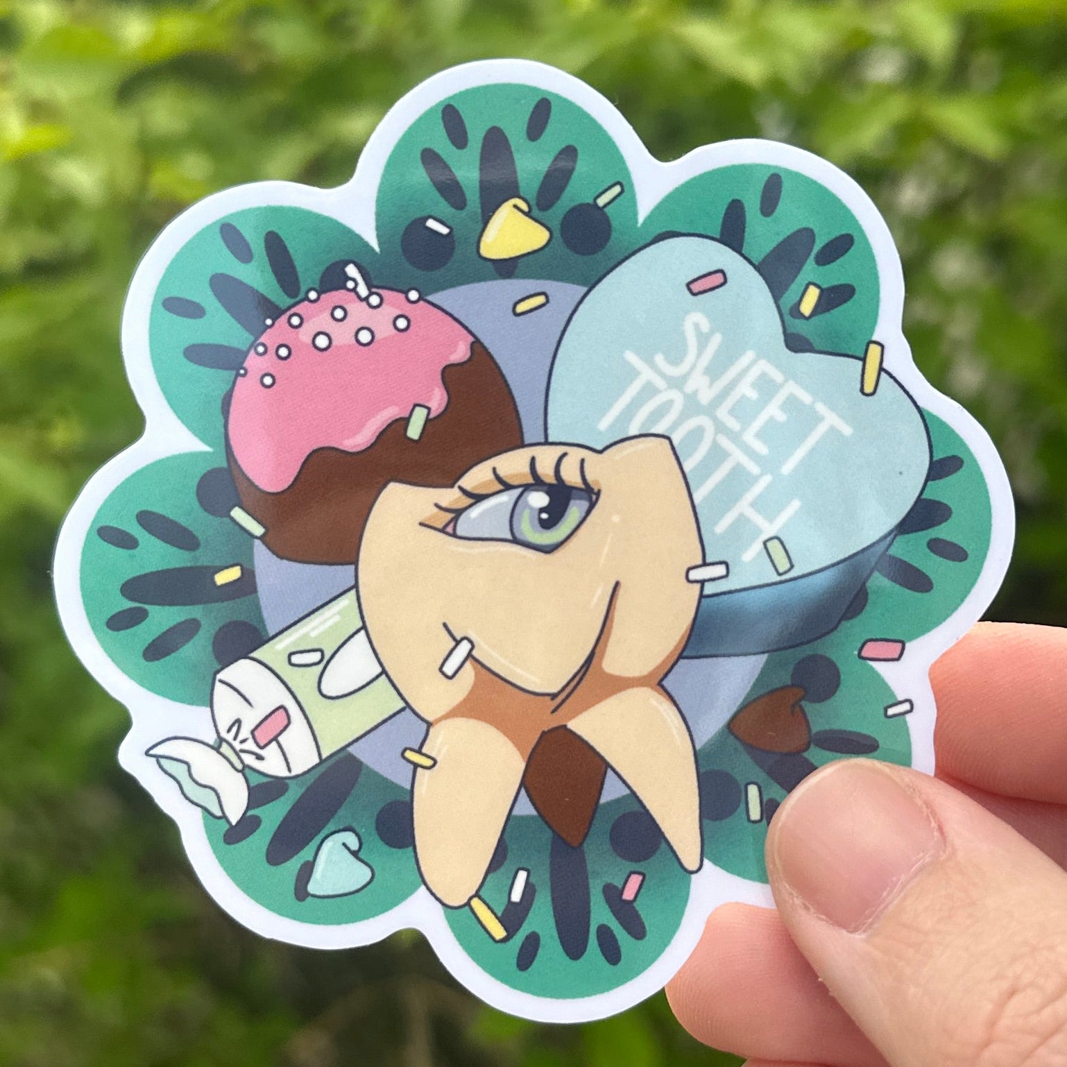 Sticker of a tooth with an eyeball surrounded by candy. background is a green bush.