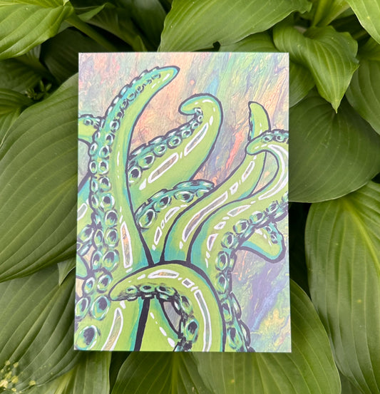 A colorful art print featuring an intricate illustration of tentacles on a glossy cardstock background, presented against a natural green leaf backdrop.