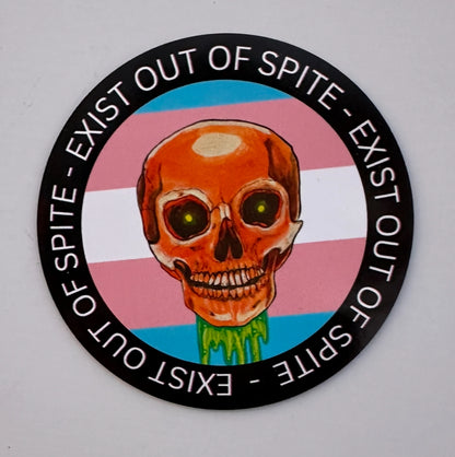 Round magnet with a skull over a transgender pride flag encircled by the text exist out of spite